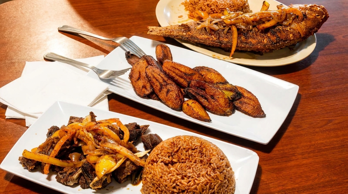 A table spread with fried fish, plantains, rice, and meat with peppers and onions.