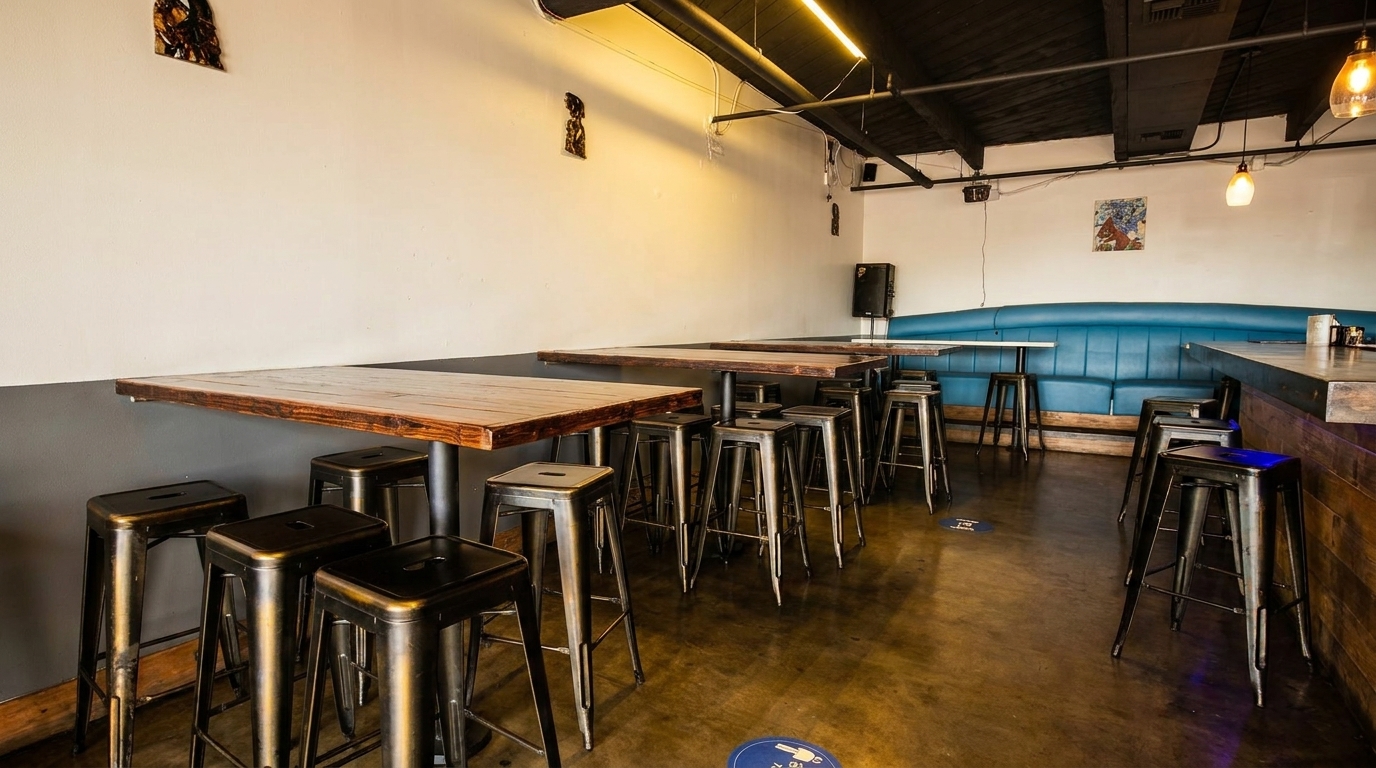 Restaurant interior with high-top tables, metal stools, a blue booth, and a wooden bar.
