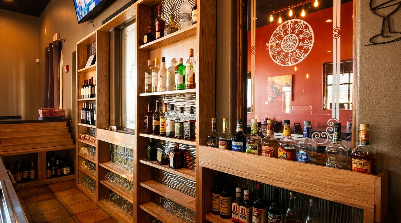 A well-stocked wooden bar area with liquor bottles, wine, and glassware, reflecting a red wall.