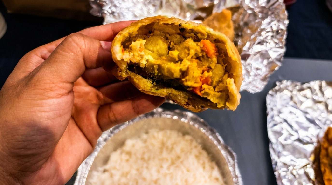 A hand holds a half-eaten samosa, revealing its savory potato and vegetable filling.