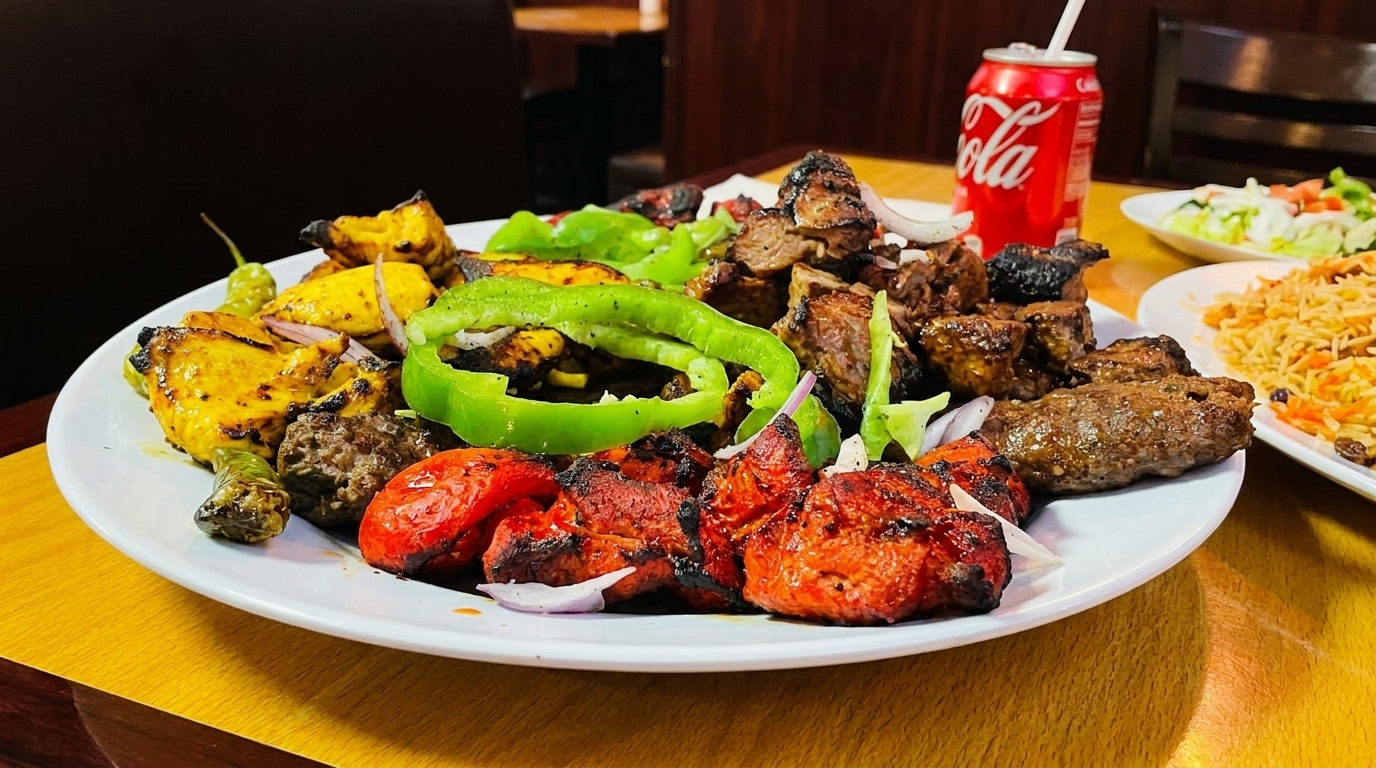 A large platter of mixed grilled meats, peppers, and onions, with rice and salad in the background.