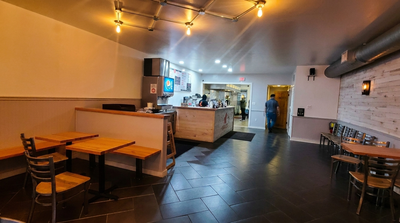 Interior of a casual restaurant with wooden tables, dark tiled floors, and a service counter.