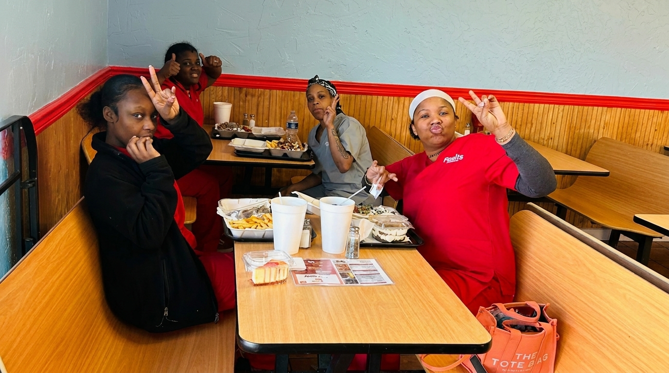 Four women in a restaurant booth posing playfully with their meals and drinks on the tables.