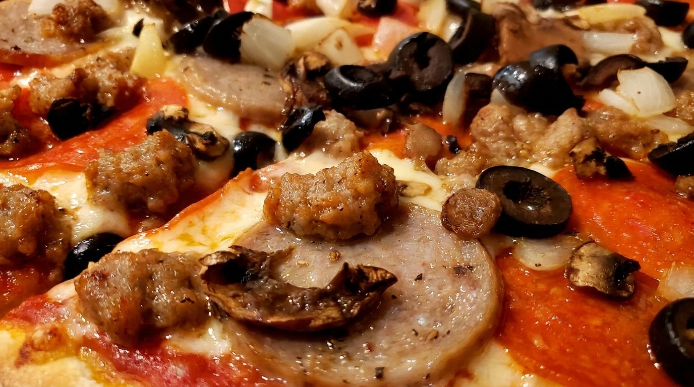 Close-up of a pizza with pepperoni, sausage, black olives, onions, and mushrooms.