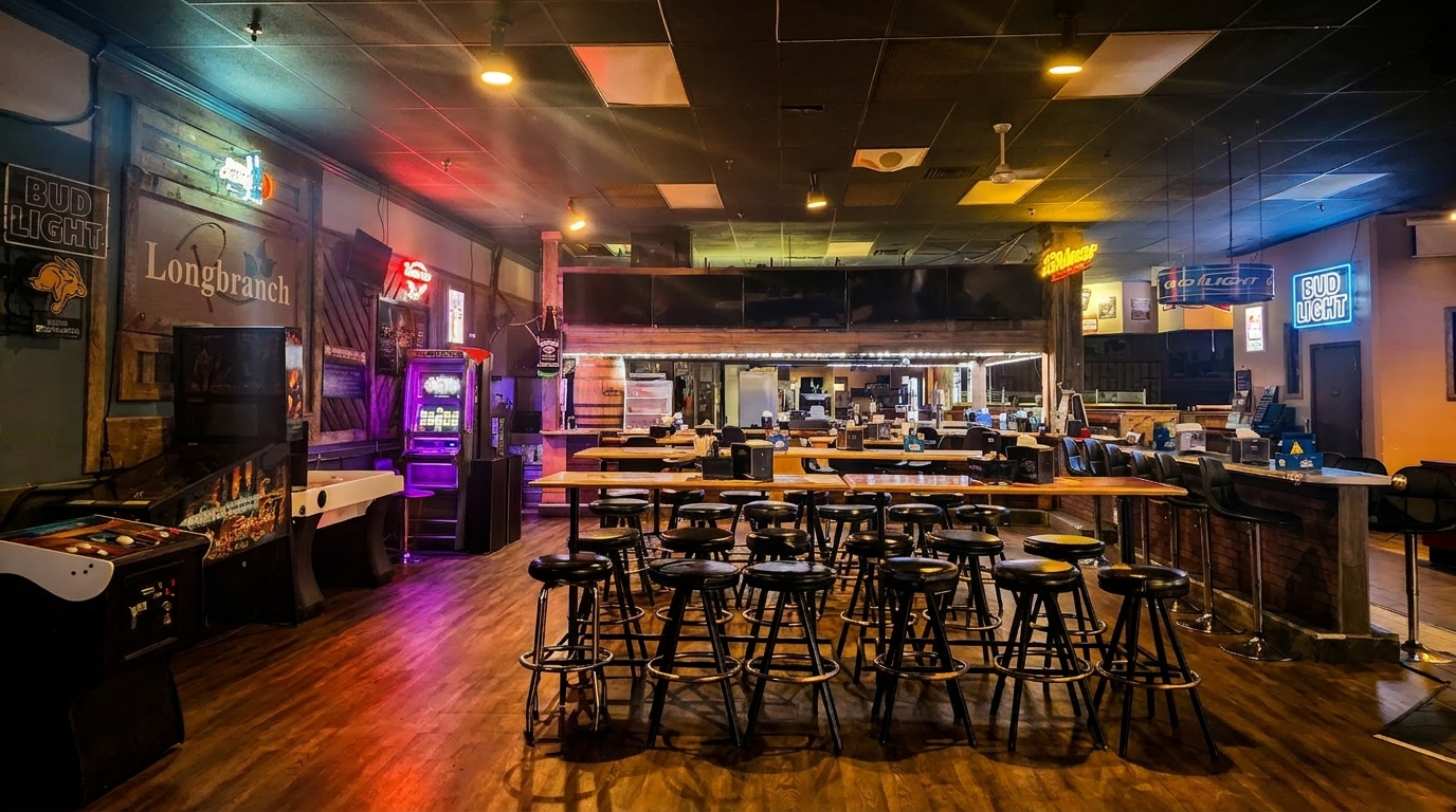 Interior of Longbranch bar with arcade games, high-top tables, and neon Bud Light signs.