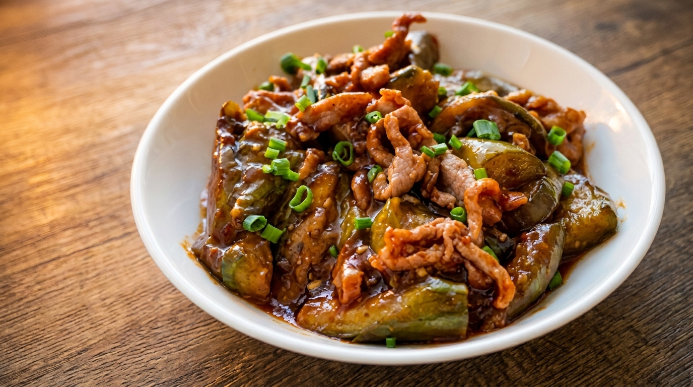 A white bowl filled with stir-fried eggplant and pork, garnished with chopped green onions.