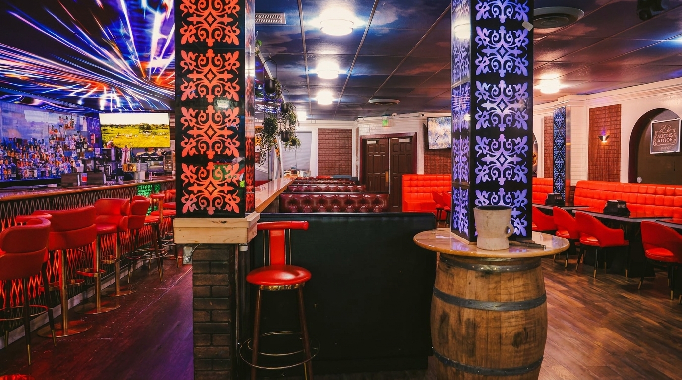 Vibrant bar interior with red bar stools, booths, and decorative pillars under a colorful, illuminated ceiling.