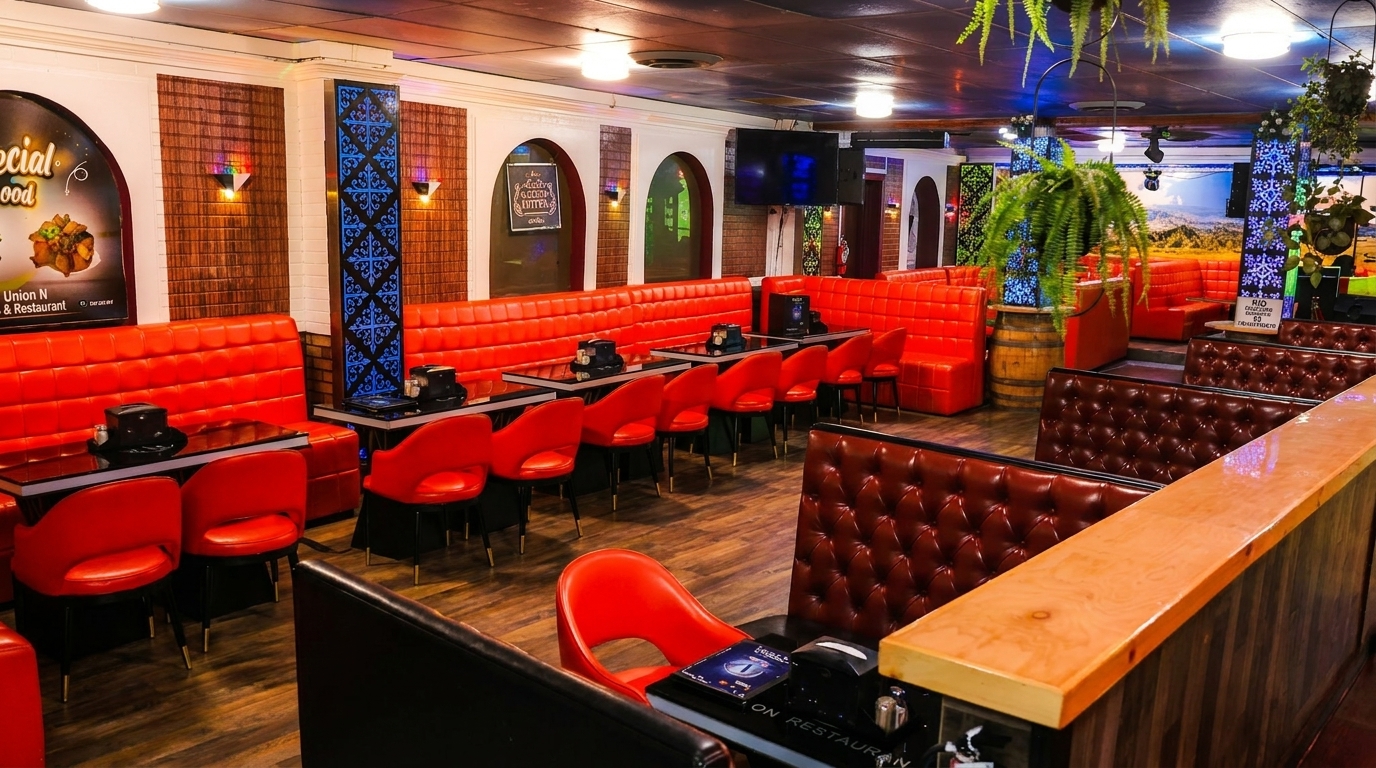 Restaurant interior with red booth seating, black tables, and decorative plants under warm lighting.