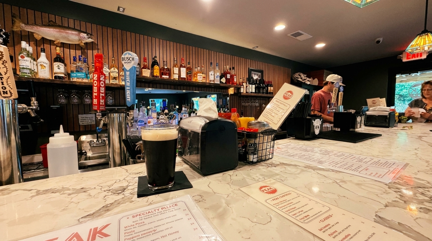A dark beer on a marble bar top with liquor bottles, a fish mount, and a bartender in the background.