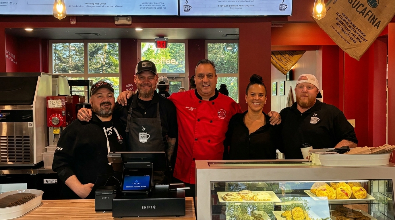 Five smiling staff members, three men and two women, pose behind a counter in a coffee shop.