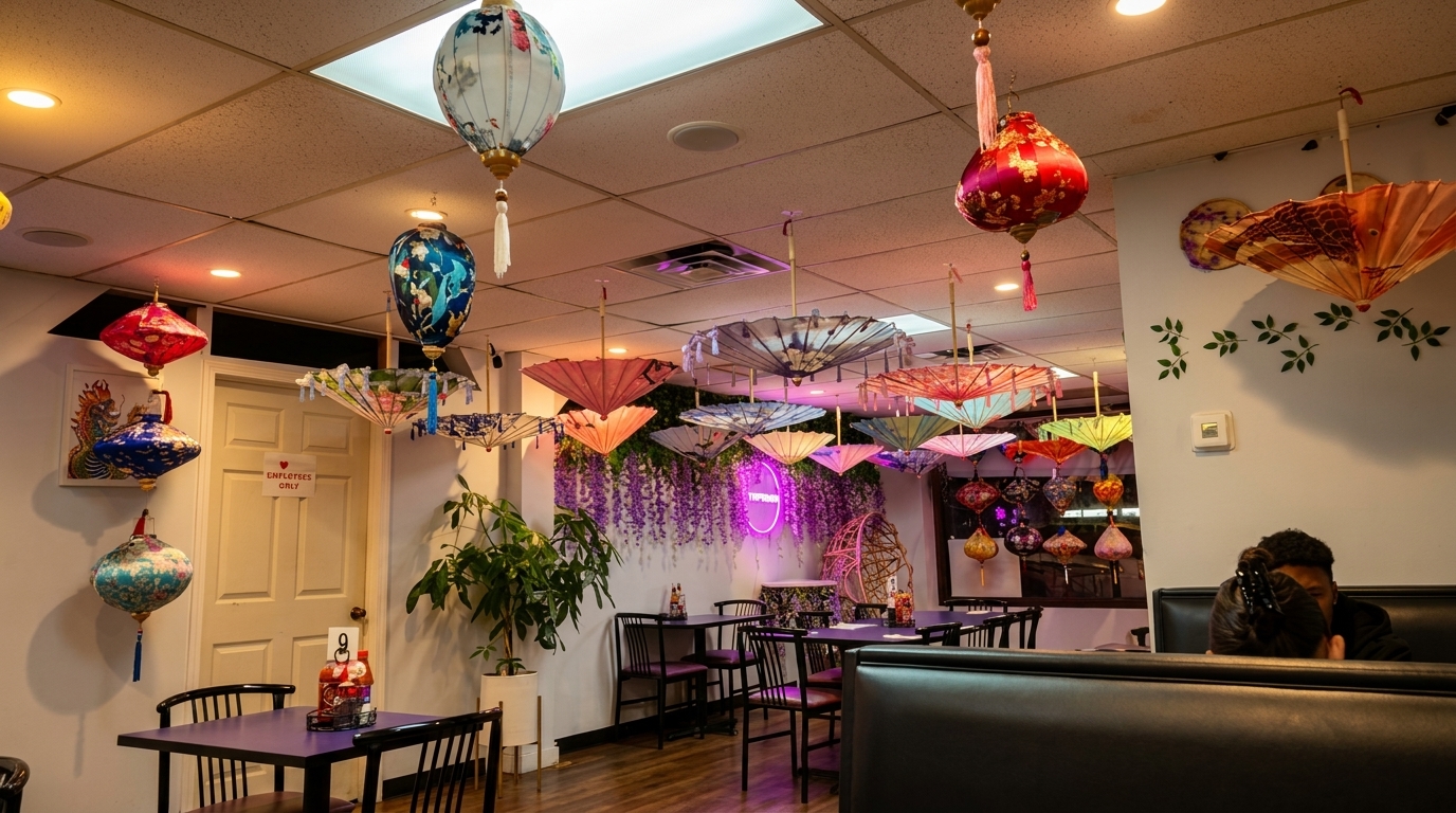 Restaurant interior with colorful lanterns and umbrellas hanging from the ceiling, and a person seated at a booth.
