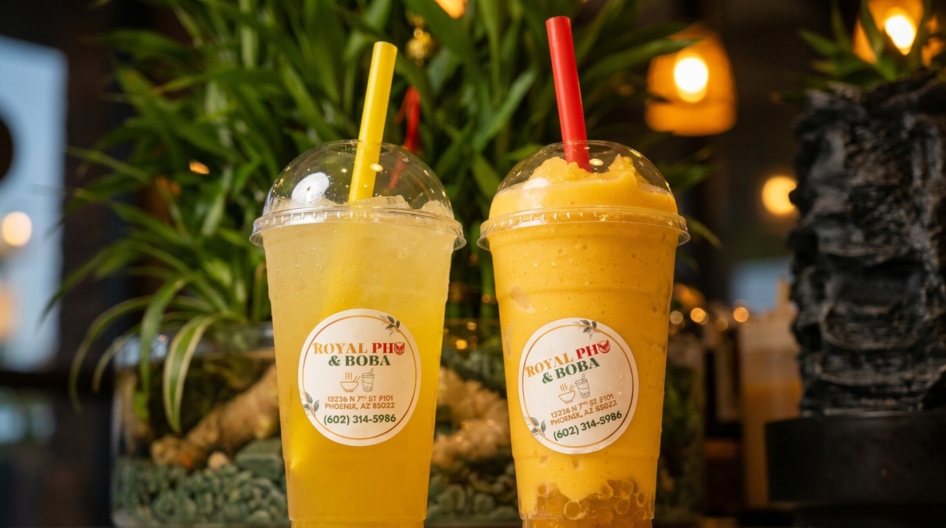 Two Royal Pho & Boba drinks, one yellow iced tea and one mango smoothie, with green plants in the background.