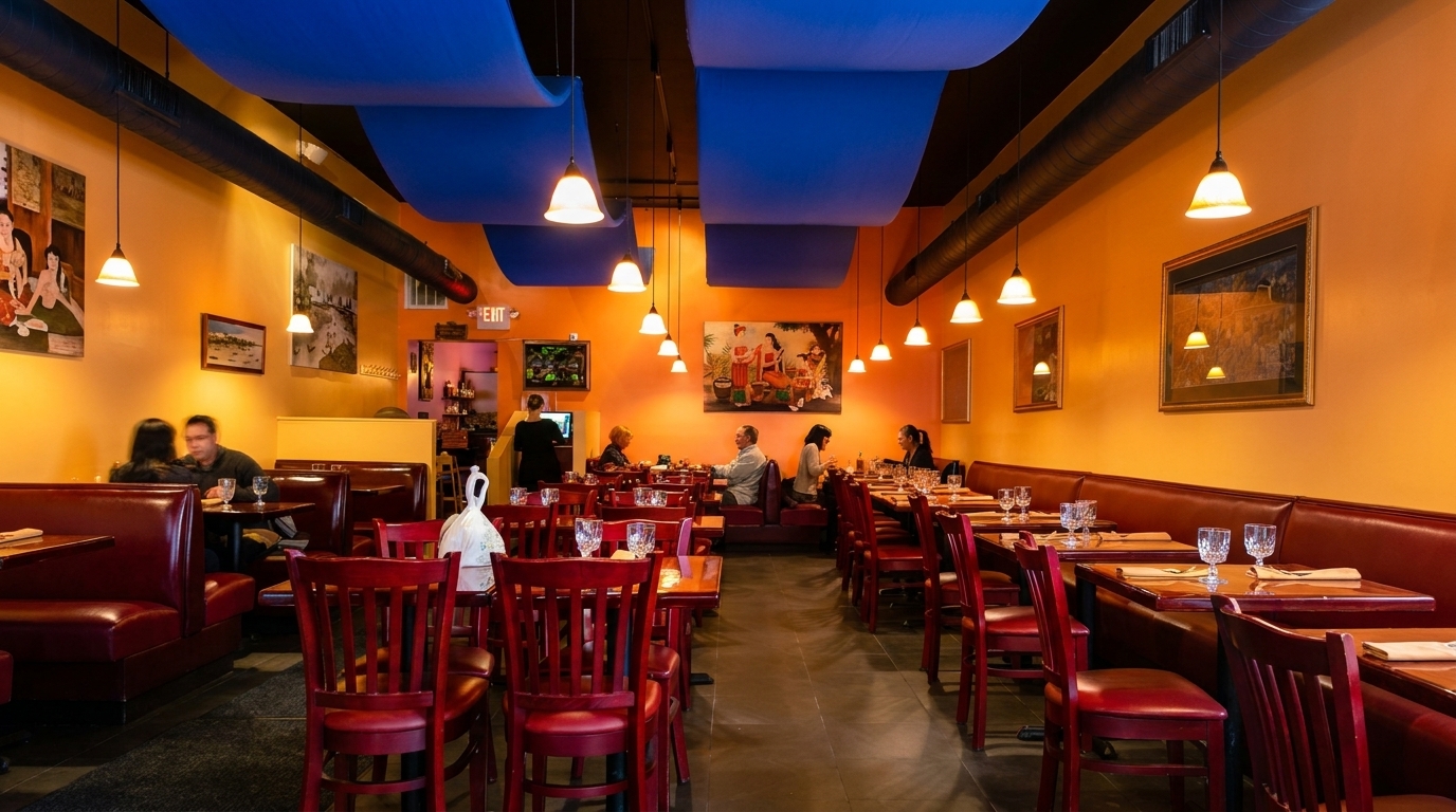 Warmly lit restaurant interior with orange walls, blue ceiling panels, red booths, and dining guests.