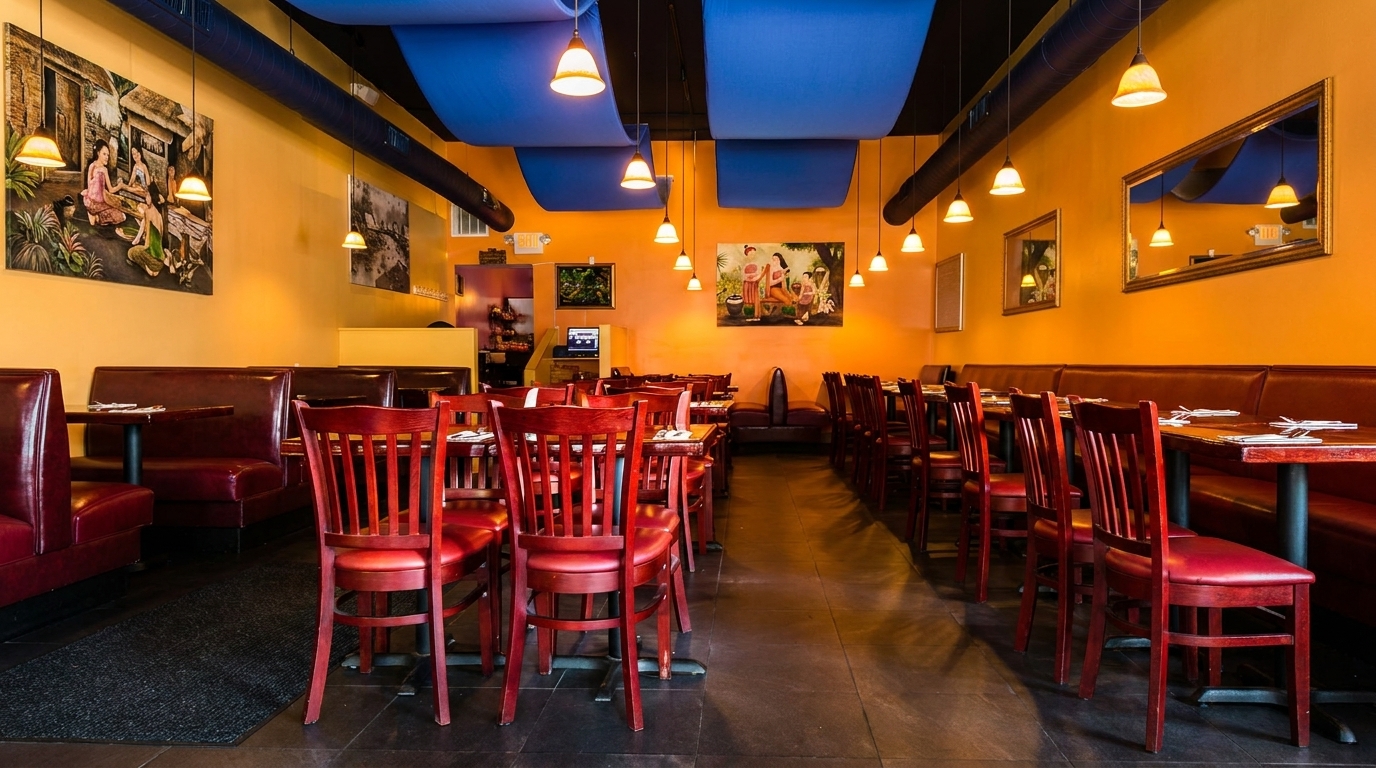 Empty restaurant interior with orange walls, blue ceiling panels, red chairs, and booth seating.