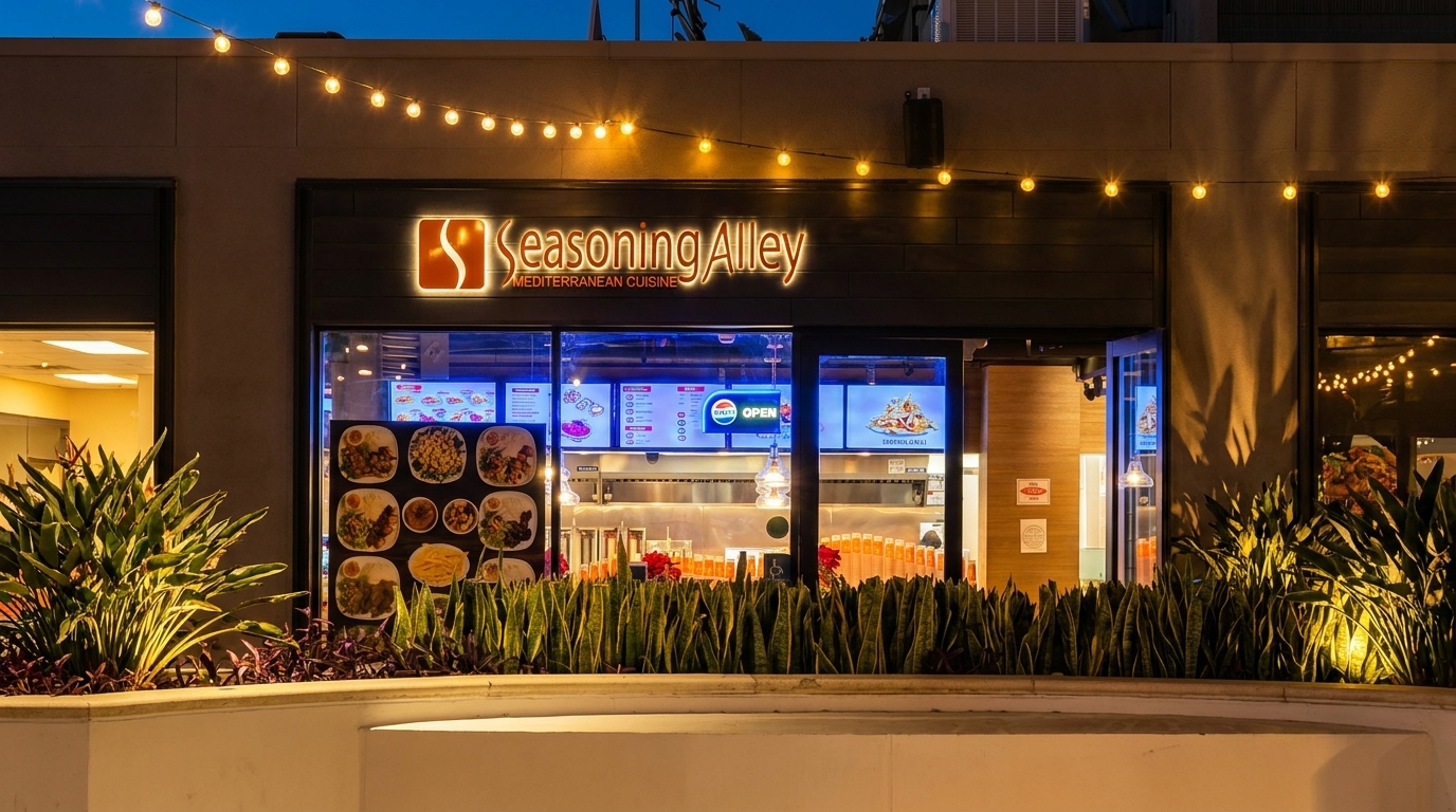 Exterior of Seasoning Alley Mediterranean Cuisine at night, with string lights and illuminated signage.