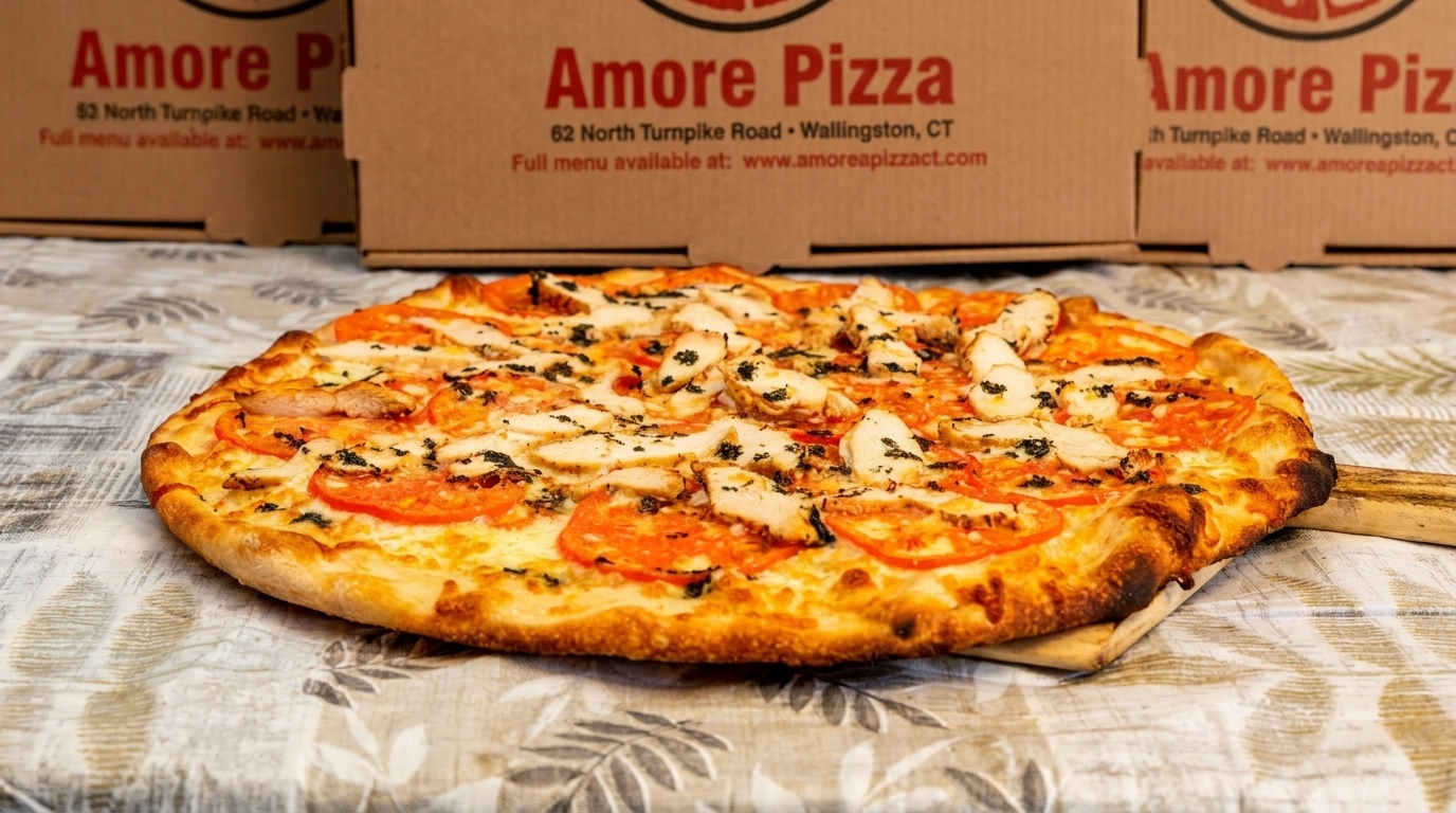 A Amore Pizza chicken and tomato pizza on a wooden peel, with pizza boxes in the background.