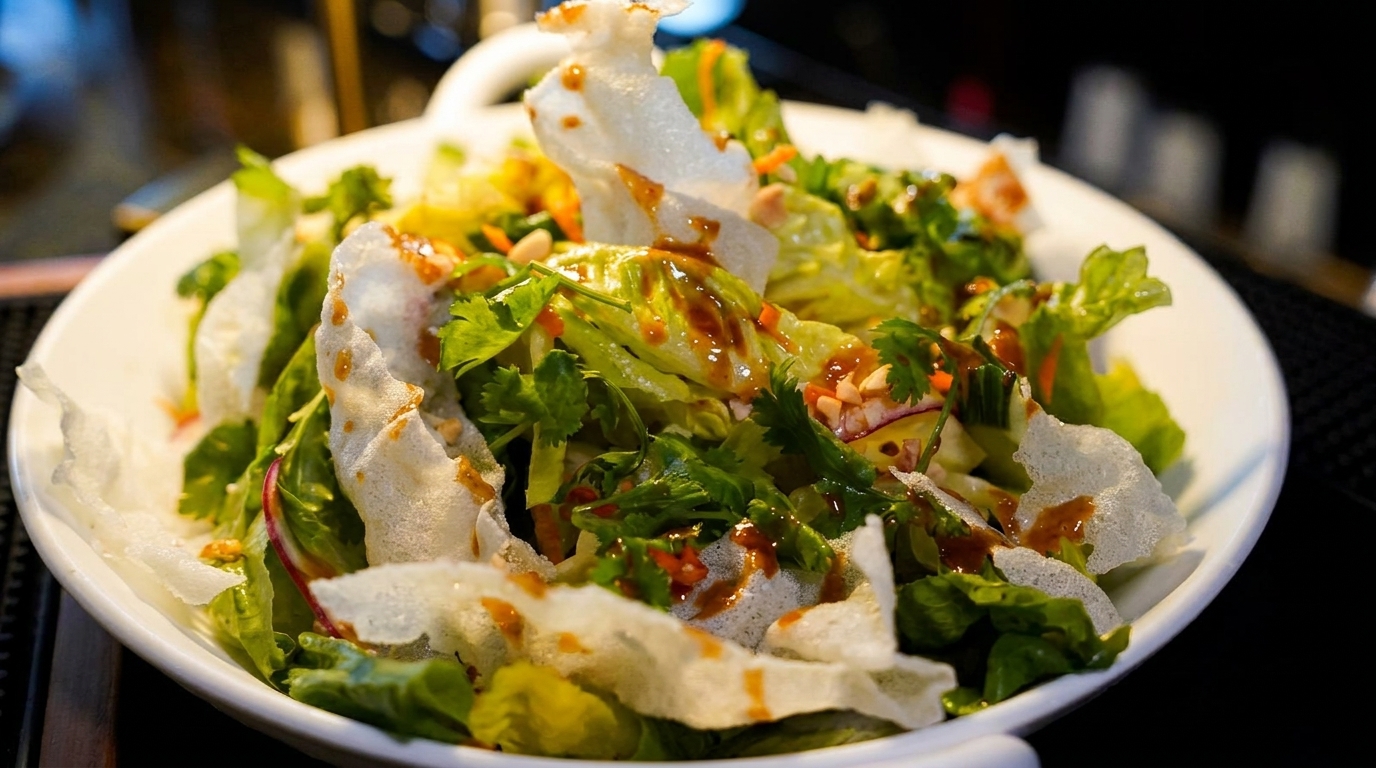 Fresh green salad with crispy rice paper, cilantro, and a savory dressing in a white bowl.