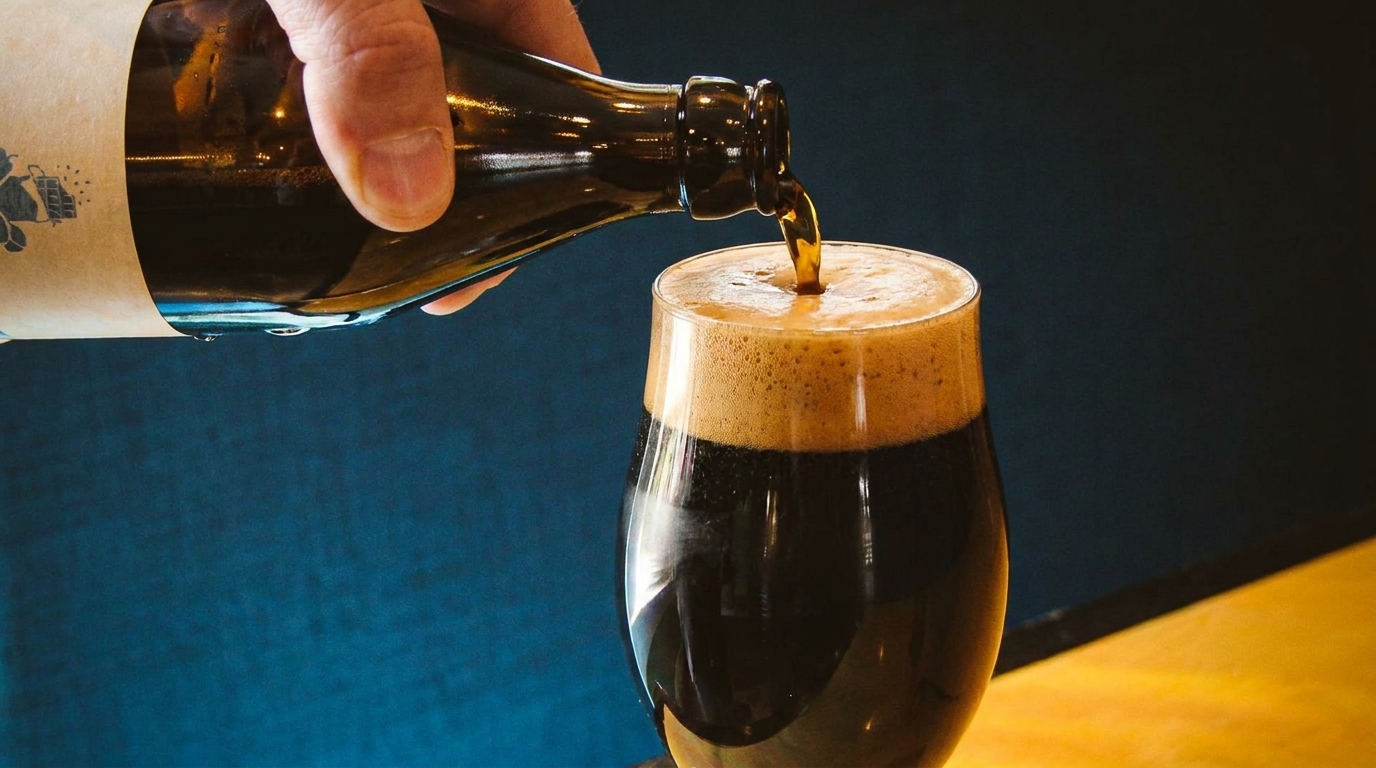 Dark beer being poured from a bottle into a glass, creating a frothy head.