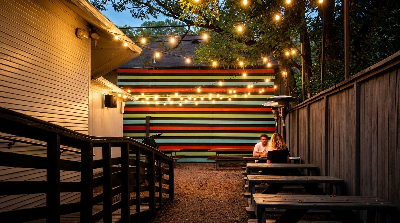 Outdoor patio at dusk with string lights, picnic tables, and two people dining.
