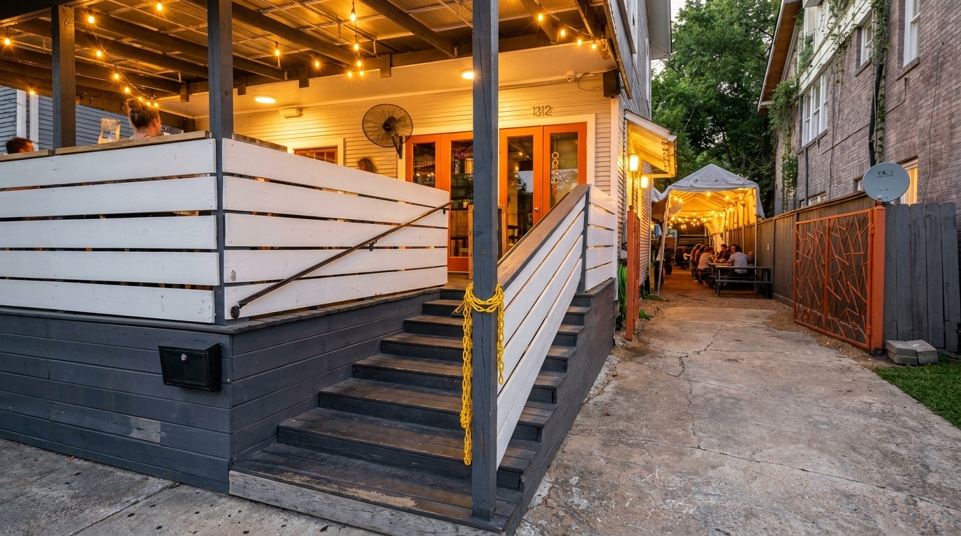 Outdoor restaurant patio with string lights, a white railing, and a side alley with covered seating.