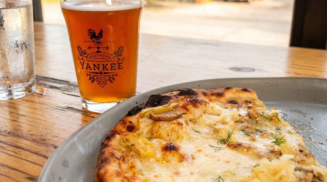 A slice of white pizza with mushrooms and dill, next to a Southern Yankee Beer Co. glass.