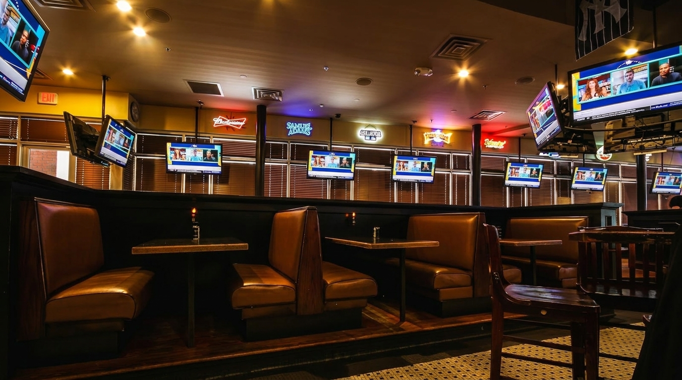 Interior view of a sports bar with multiple TVs showing sports, brown booths, and neon signs.