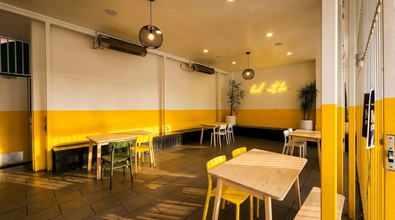 Bright, modern restaurant interior with yellow and white walls, light wood tables, and colorful chairs.