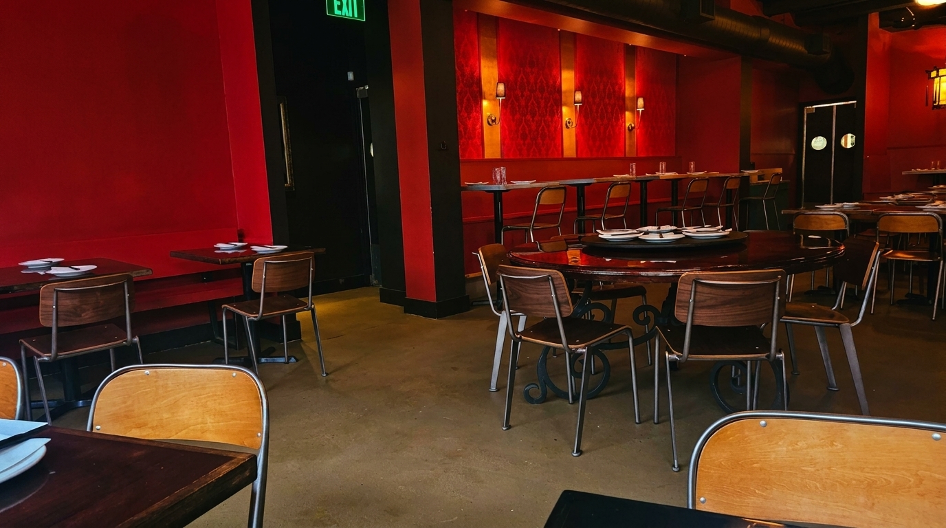 A restaurant dining room with red walls, dark tables, and wooden chairs, featuring a large round table.