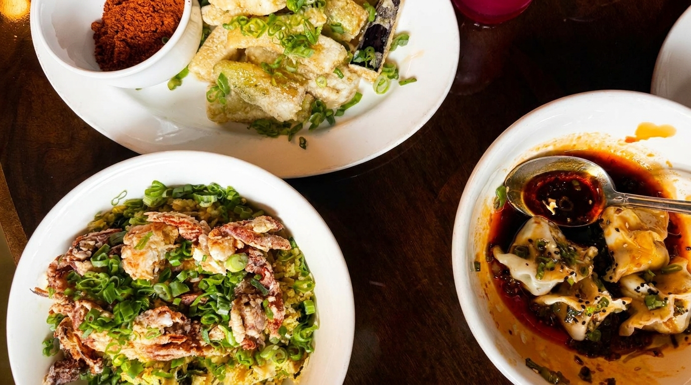 Three bowls of Asian dishes, including dumplings in chili oil, fried soft-shell crab, and fried eggplant.
