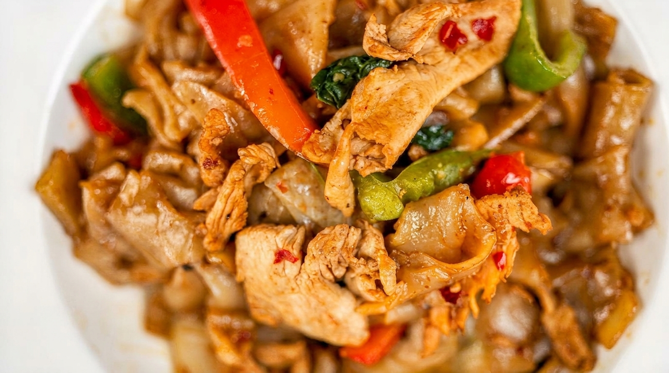 Close-up of Pad See Ew with chicken, wide noodles, red and green bell peppers, and basil.