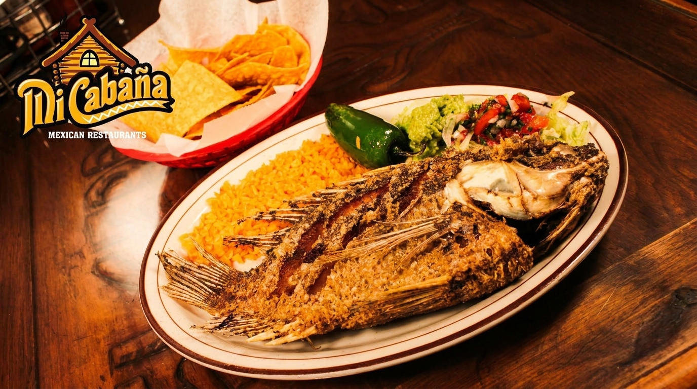 Whole fried fish with rice, guacamole, pico de gallo, and a jalapeño on a wooden table.