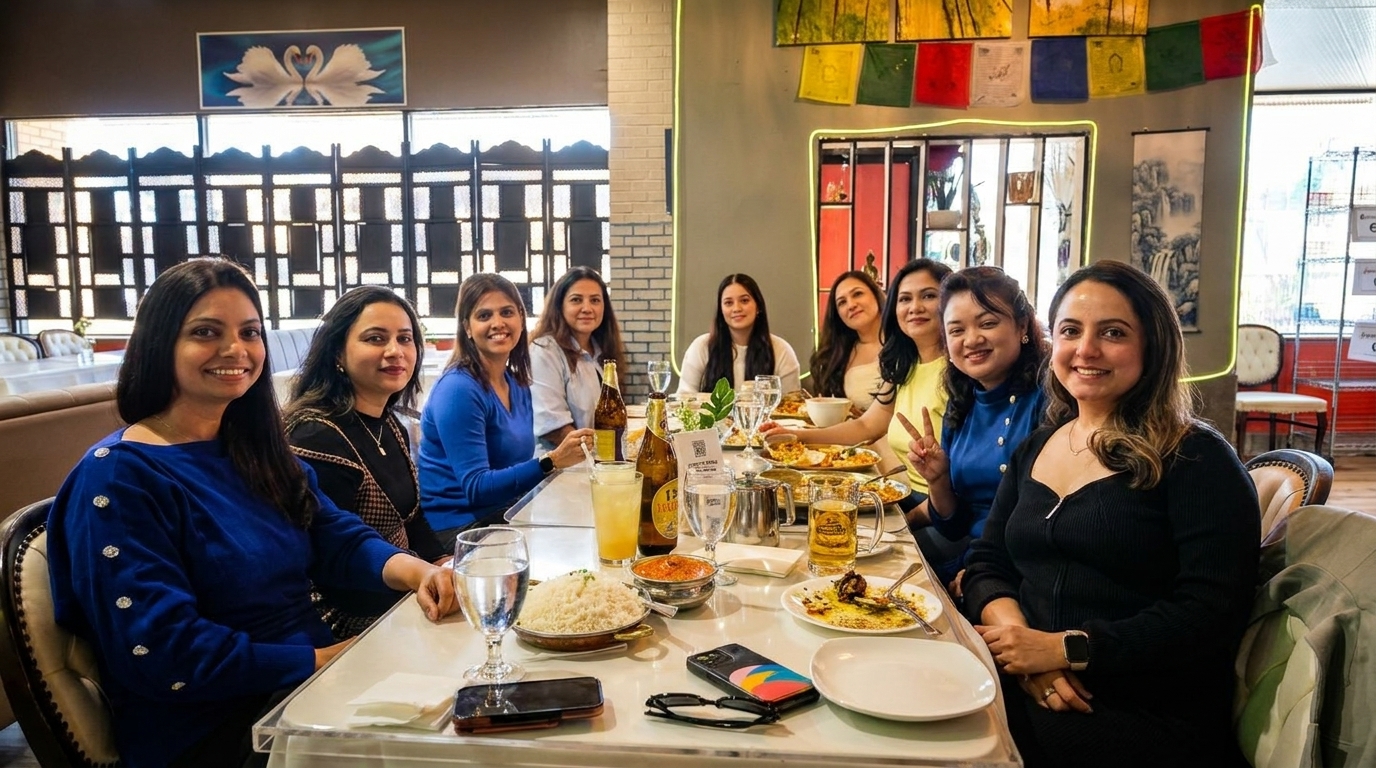 Eight women smiling and dining together at a long table in a restaurant.