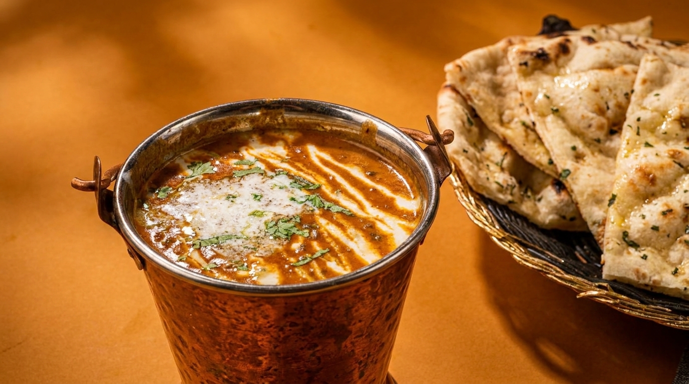 Indian dal makhani in a copper pot with cream and cilantro, alongside a basket of naan.