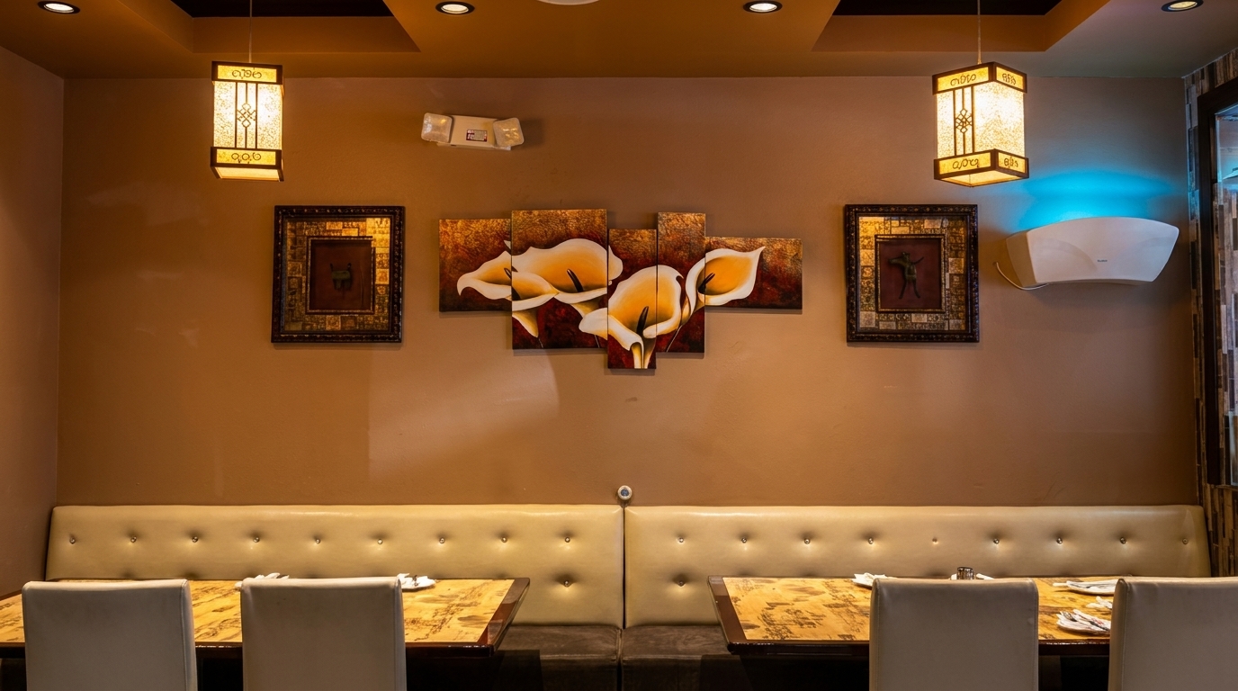 Restaurant interior with light brown walls, cream booths, and tables set, featuring decorative art and lighting.
