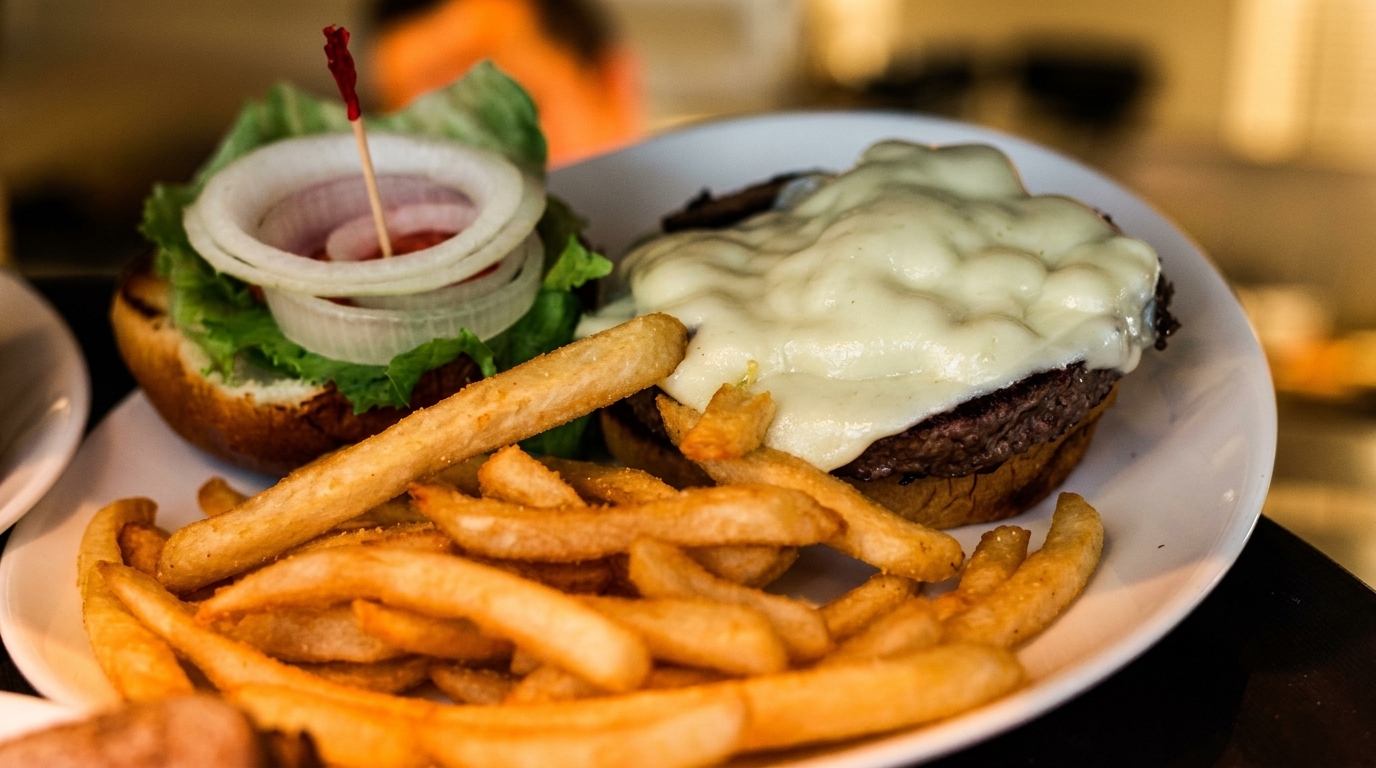 A juicy cheeseburger with melted white cheese, lettuce, and onion rings, served with golden fries.