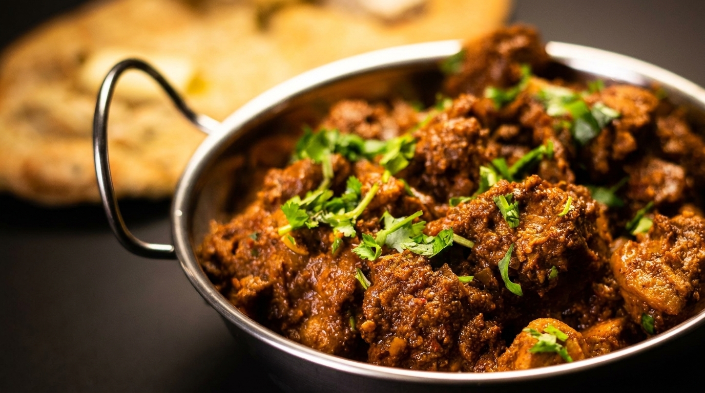 Close-up of a metal bowl filled with rich, brown curry, garnished with fresh green cilantro.
