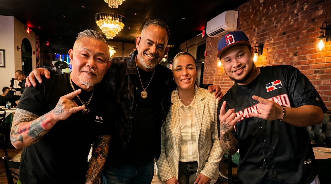 Four smiling people, two men with tattoos, a woman, and a man in a baseball jersey, pose indoors.