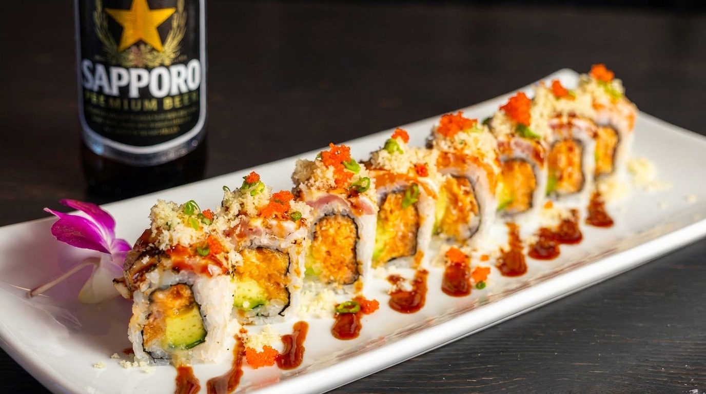 Sushi roll platter with avocado, roe, and sauce, next to a Sapporo beer bottle.