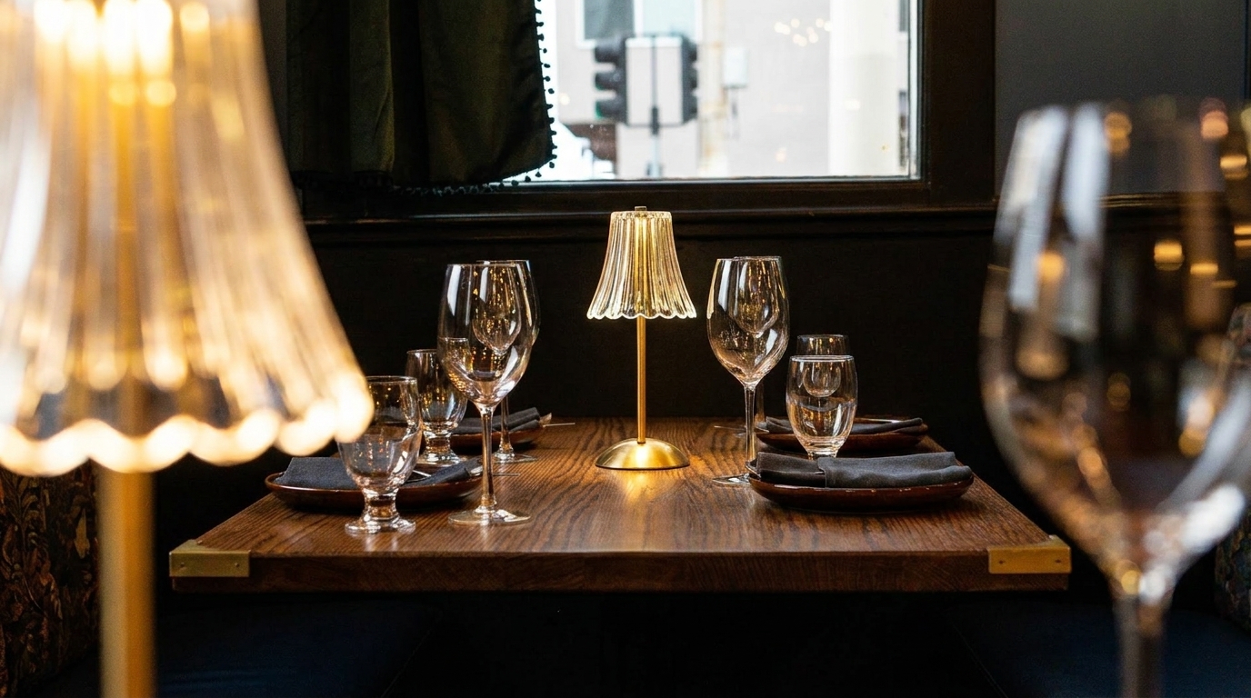 A warmly lit restaurant table set with wine glasses, water glasses, plates, and a small lamp.