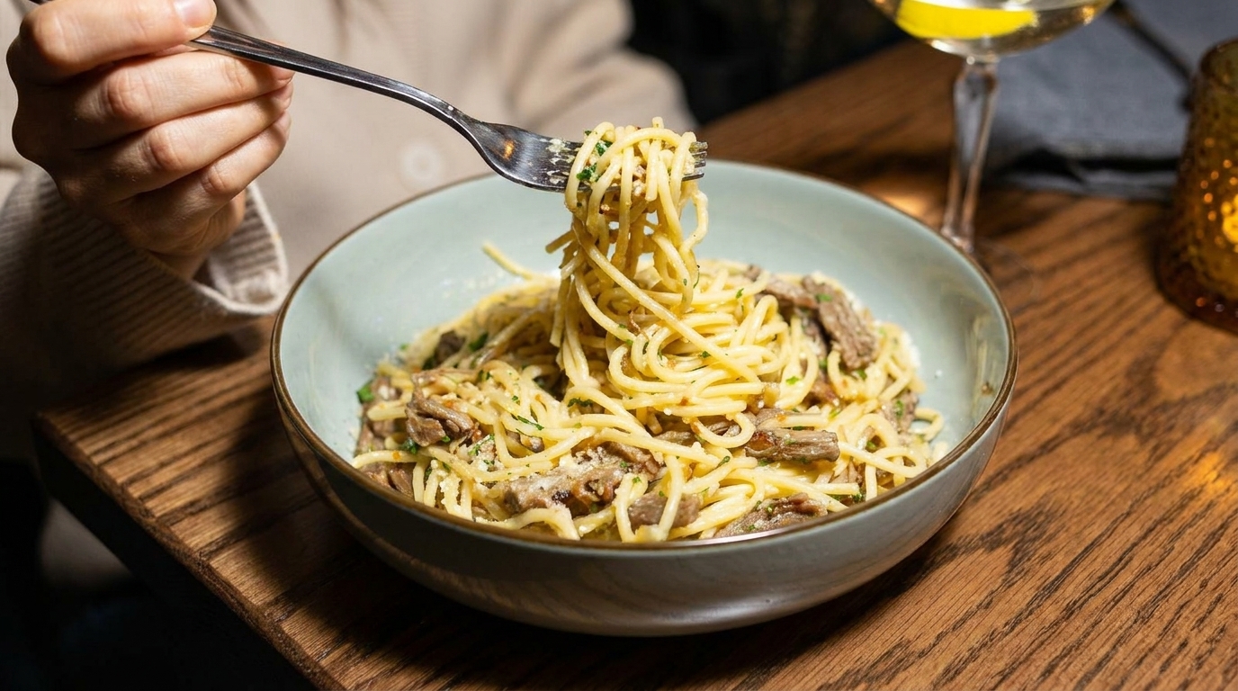 A person twirls spaghetti with meat and cheese from a light blue bowl onto a fork.