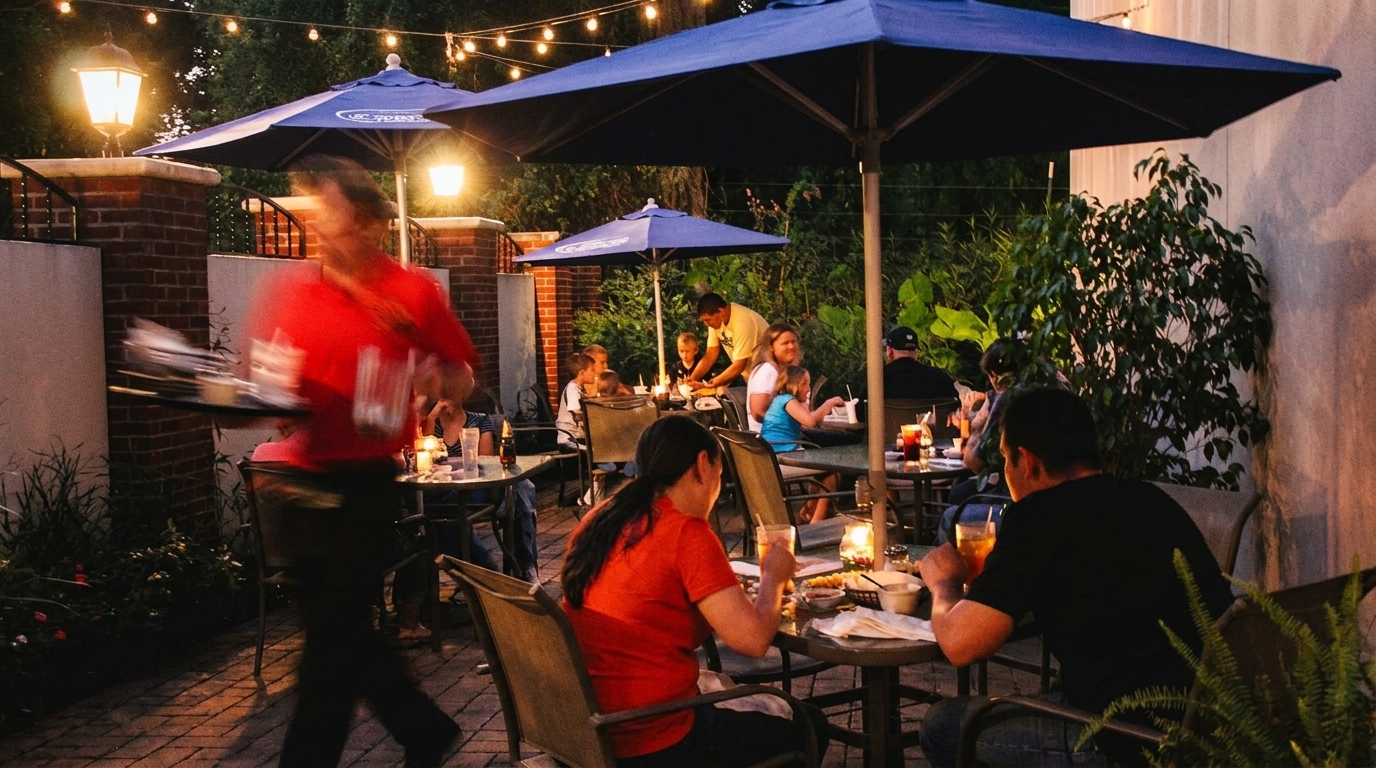 Diners enjoy an evening on a restaurant patio with blue umbrellas and string lights.
