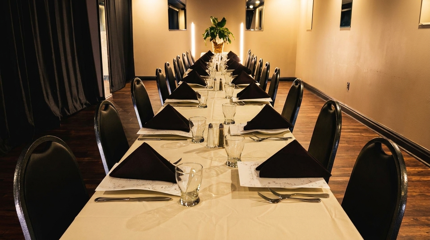 Long dining table set with black napkins and chairs, with a plant centerpiece in a private room.