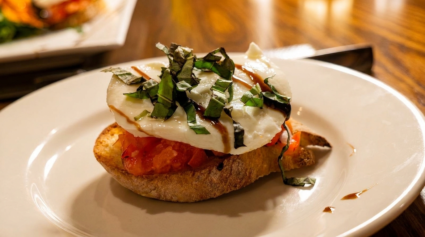 Bruschetta with fresh mozzarella, diced tomatoes, basil, and balsamic glaze on a white plate.