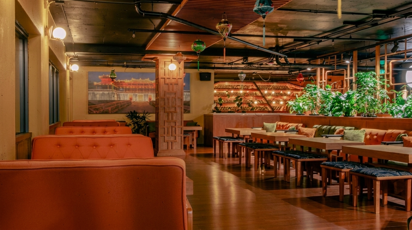 Restaurant interior with orange booths, wooden tables, green plants, and hanging lanterns.