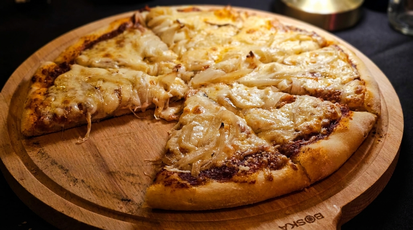 A cheesy pizza with caramelized onions, one slice removed, on a wooden serving board.