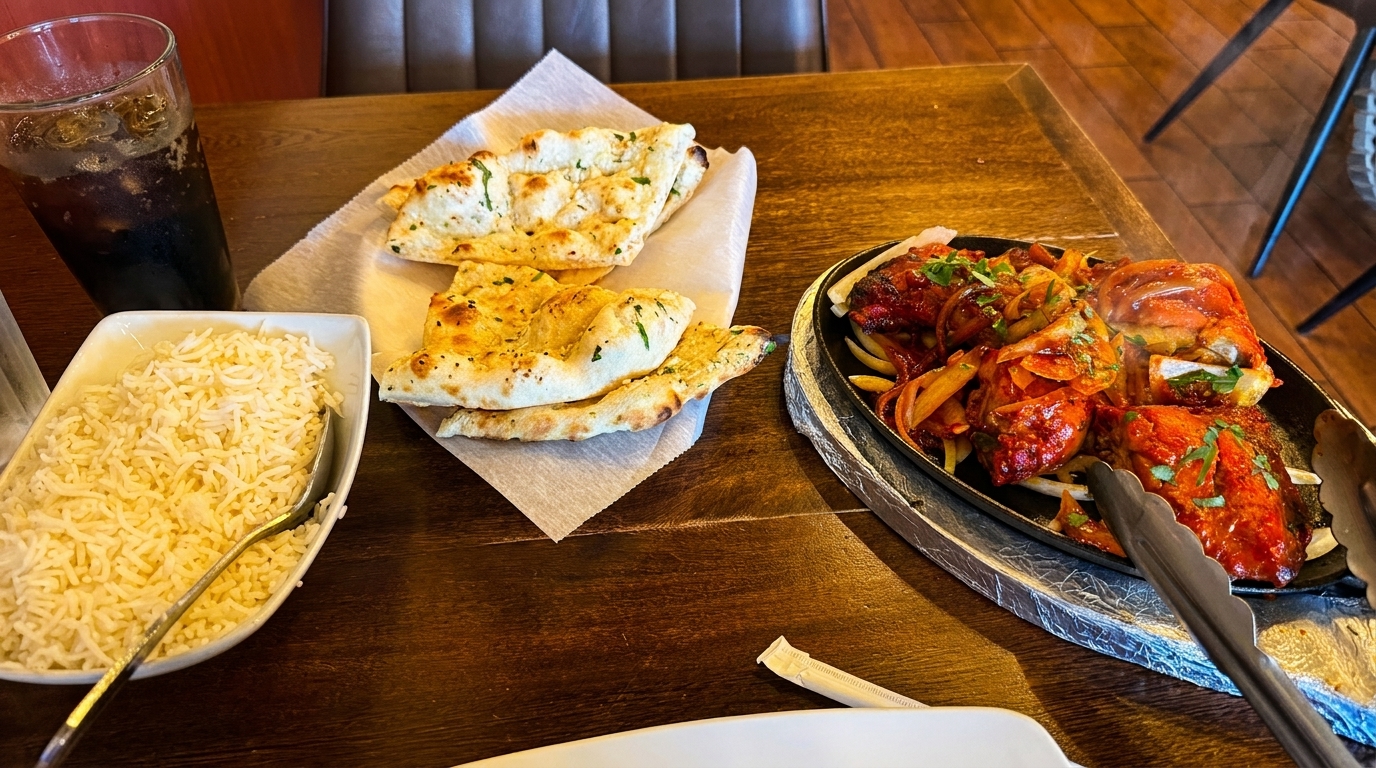 Indian food on a wooden table, including naan, rice, and a sizzling platter of tandoori chicken.