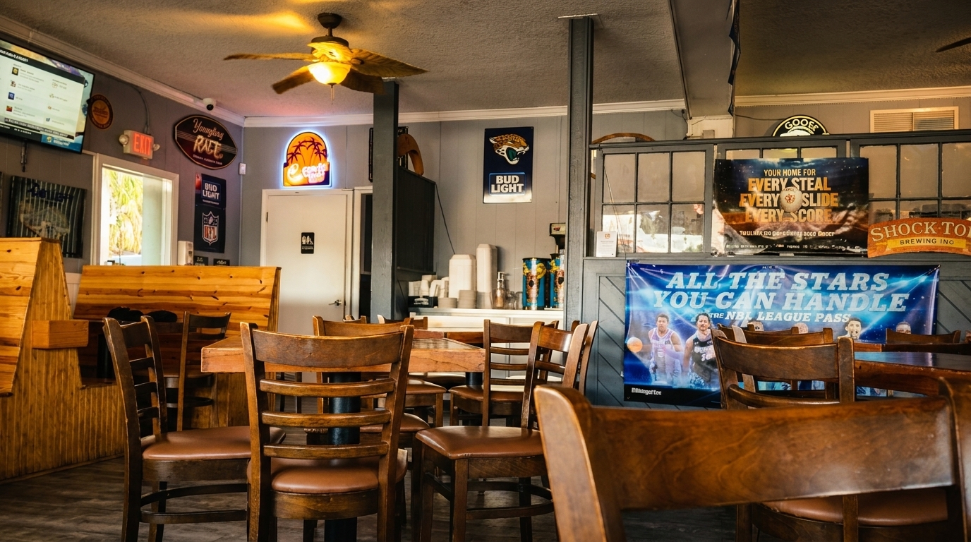 Interior of a casual restaurant with wooden tables and chairs, sports banners, and a ceiling fan.