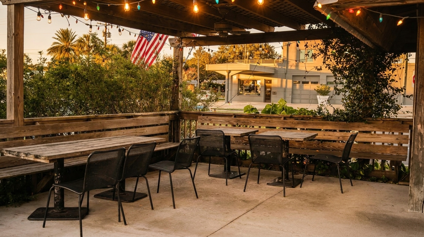 Outdoor patio with wooden tables and benches, black metal chairs, string lights, and an American flag.