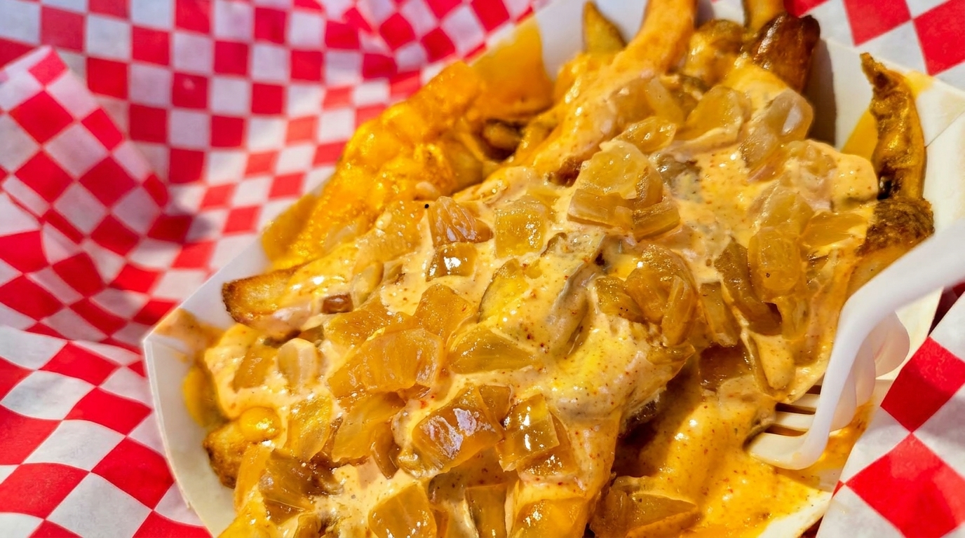 Close-up of golden french fries smothered in creamy sauce and caramelized onions, served in a paper tray.
