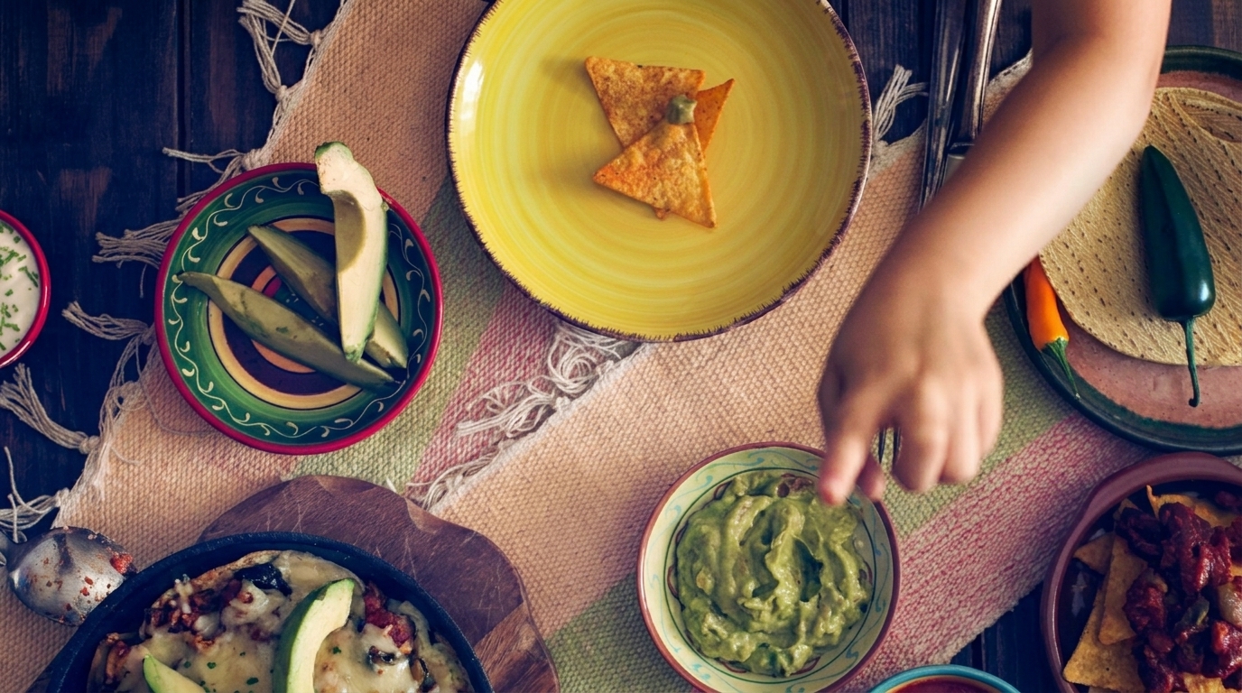 Overhead view of a person's hand reaching for guacamole on a table with various Mexican dishes.